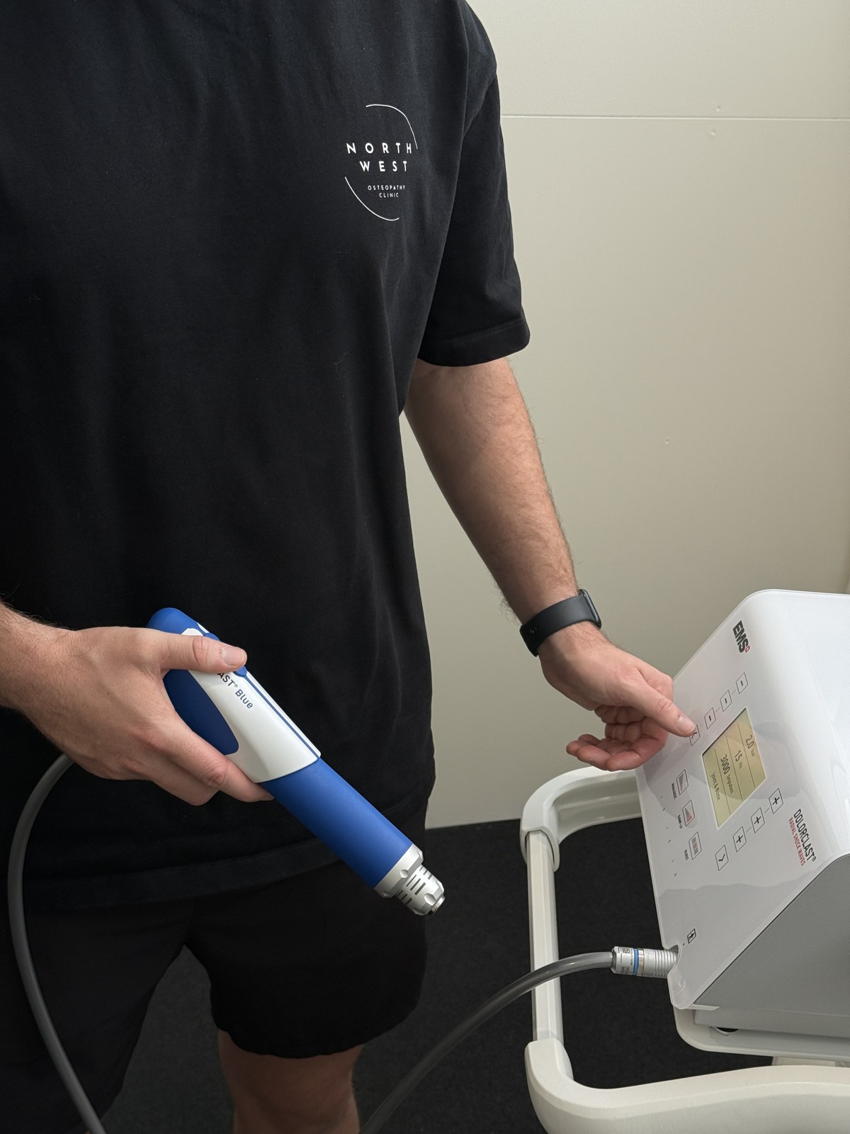 Brayden holding the shockwave handpiece and adjusting the clinic’s EMS DolorClast equipment
